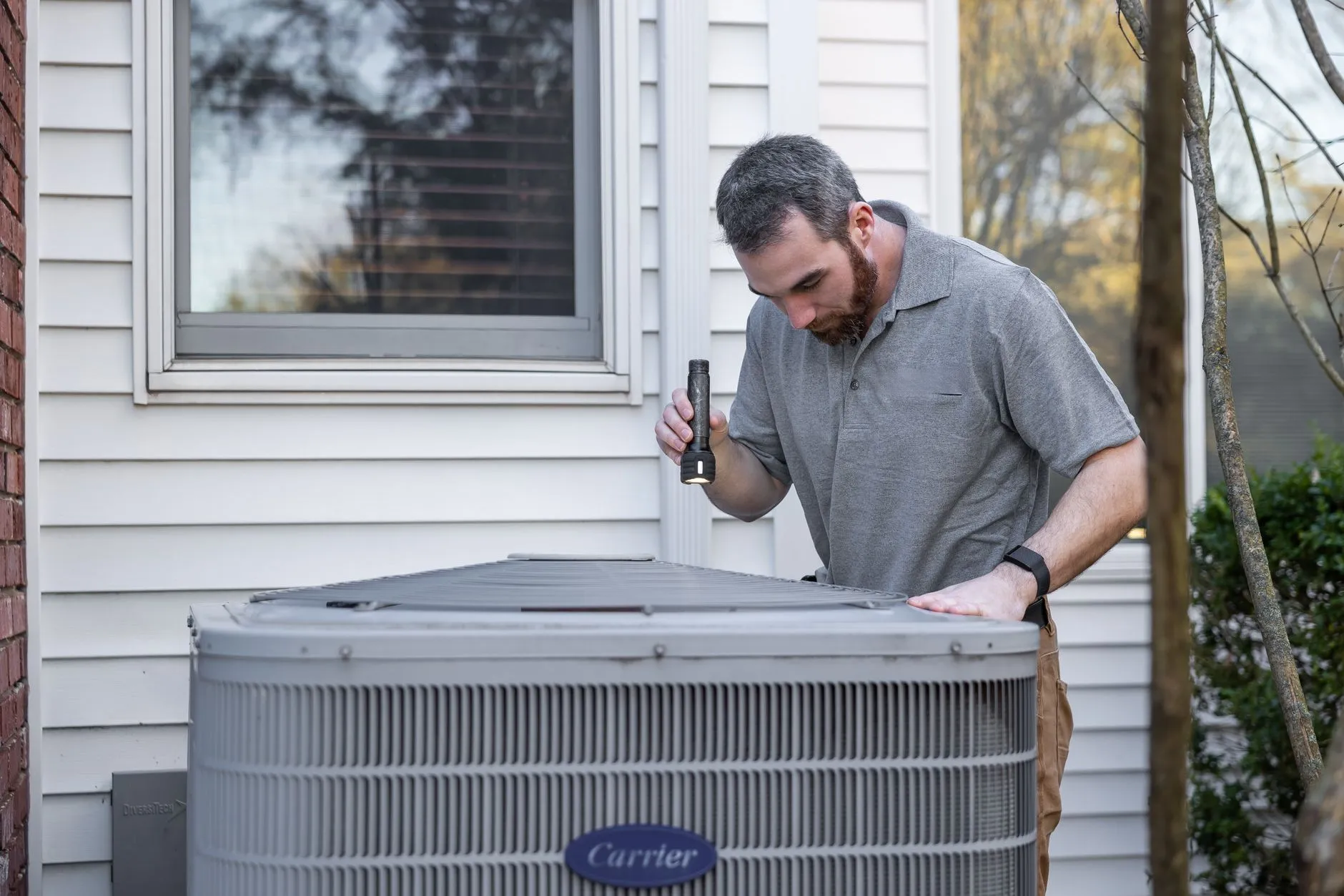 Technician inspecting an outdoor HVAC condenser unit