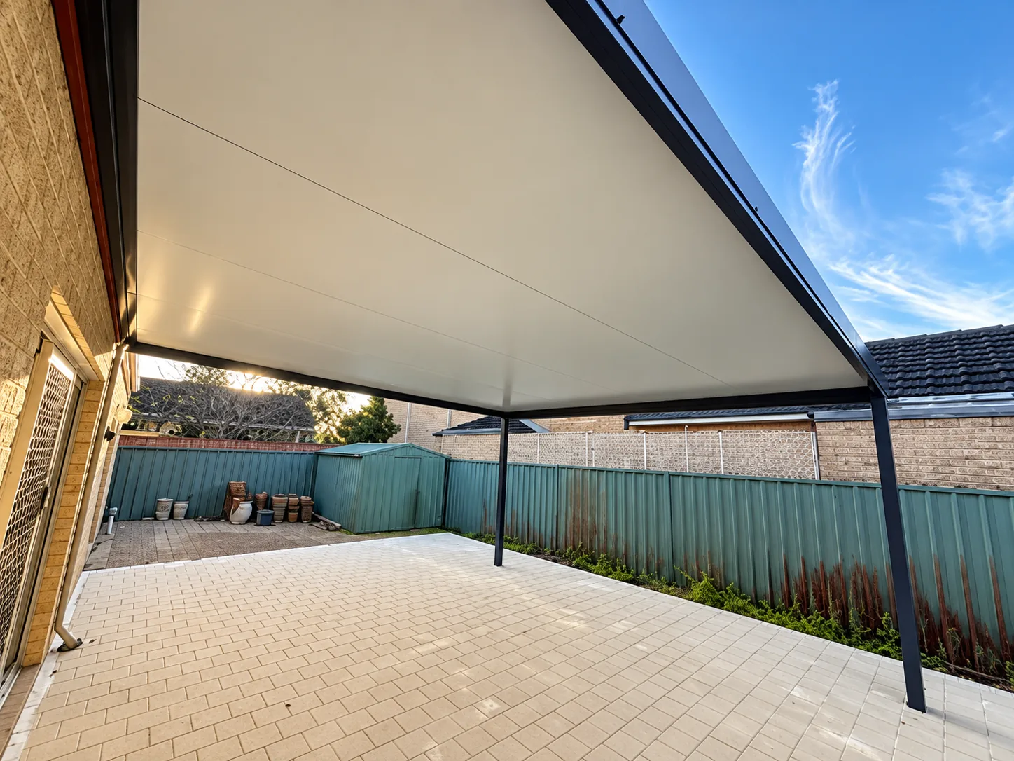 Modern alfresco patio roof extension over a spacious paved backyard area.