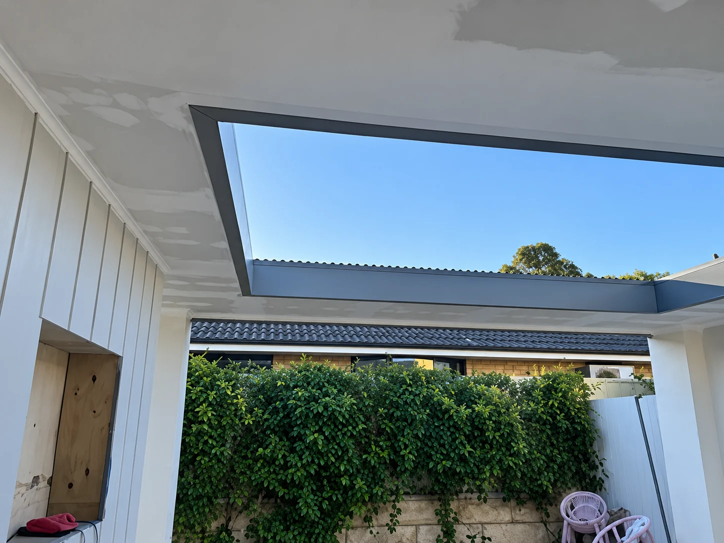 Covered patio roof renovation with an open skylight and garden outlook.