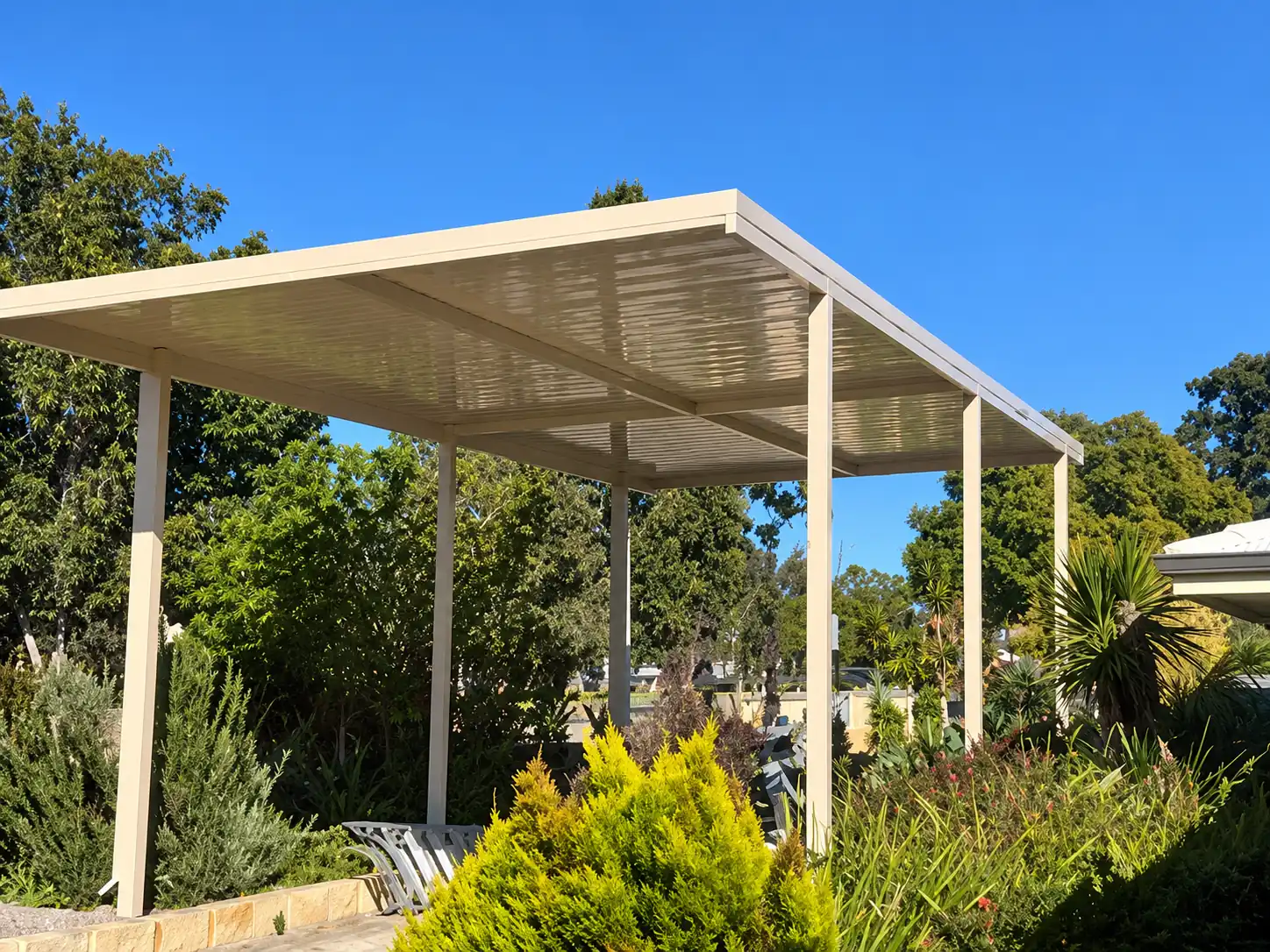 Freestanding garden carport installation surrounded by landscaped greenery.