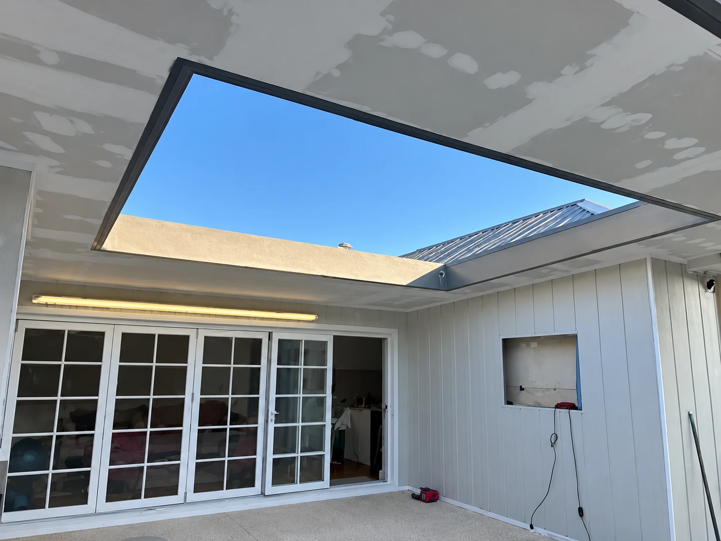 Alfresco patio renovation with a large skylight opening and white-framed doors.