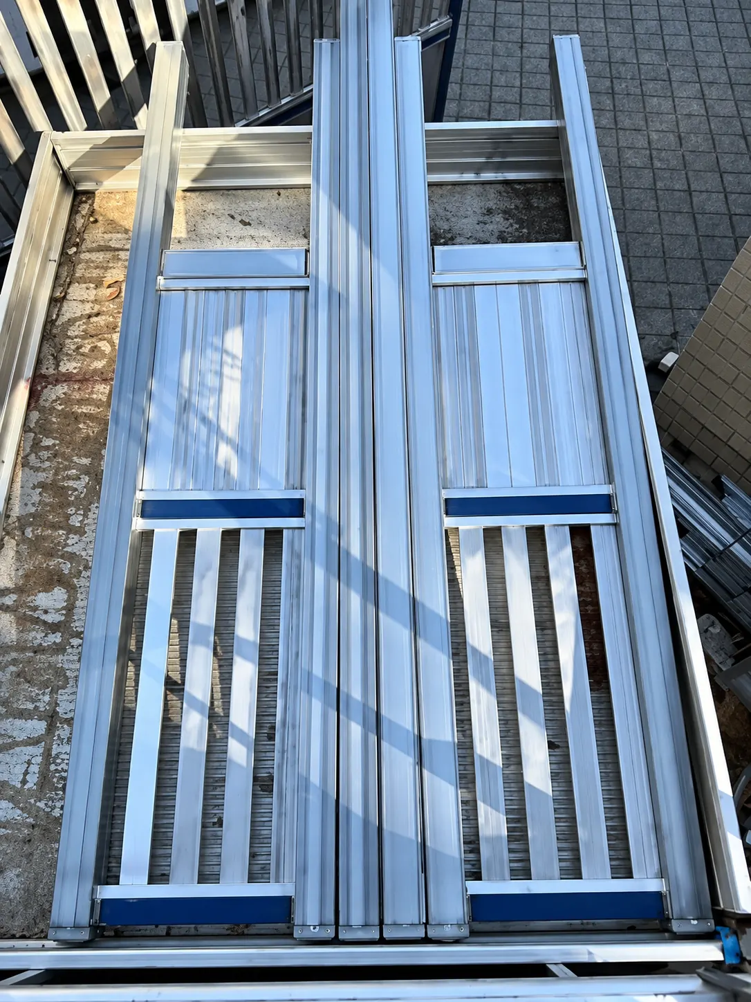 Top-down view of stacked aluminium railing panels with vertical slats in an outdoor workspace.