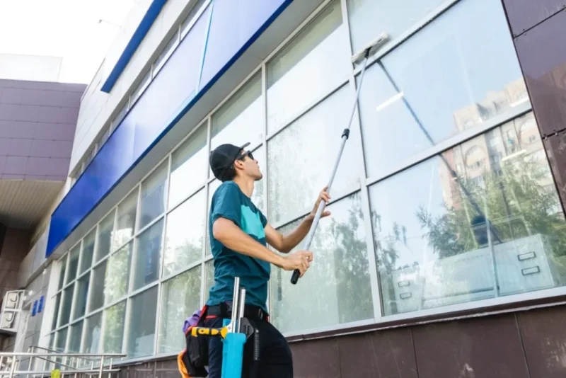 Professional window cleaner on ladder cleaning large residential windows with squeegee tool